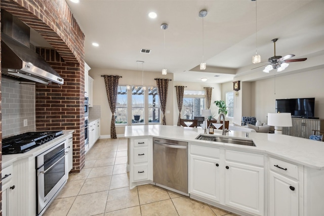 kitchen featuring a sink, wall chimney range hood, open floor plan, appliances with stainless steel finishes, and light countertops