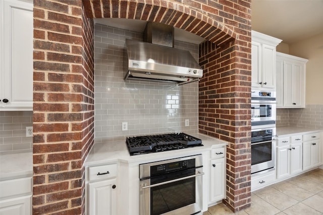 kitchen with stainless steel double oven, light countertops, black gas cooktop, wall chimney exhaust hood, and backsplash