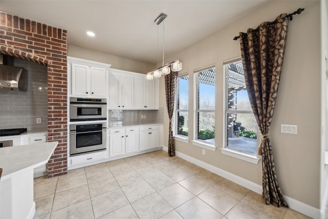 kitchen with white cabinets, wall chimney exhaust hood, tasteful backsplash, and stainless steel double oven