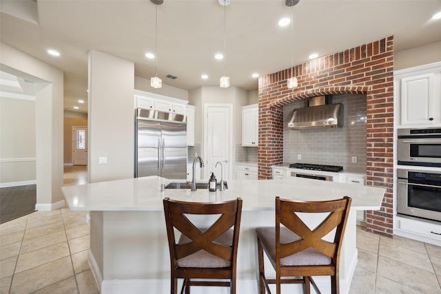 kitchen with a sink, wall chimney range hood, backsplash, stainless steel appliances, and light countertops