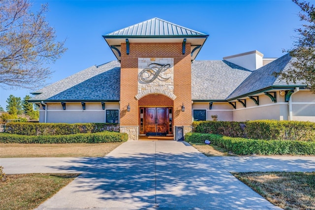 view of front of property with a standing seam roof, stone siding, roof with shingles, metal roof, and brick siding