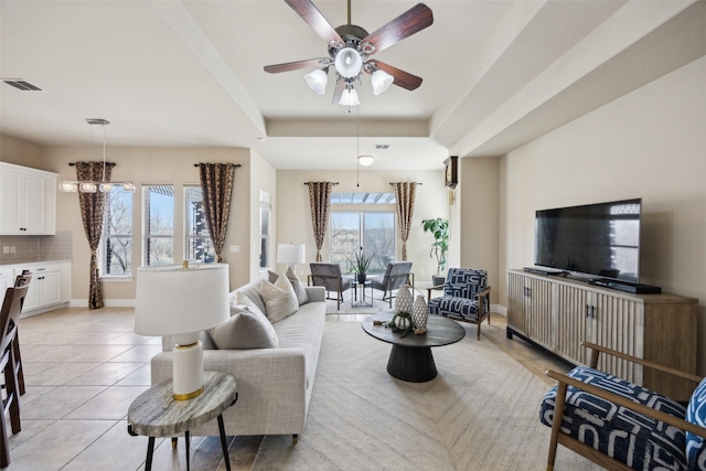 living area with light tile patterned floors, visible vents, a raised ceiling, and baseboards