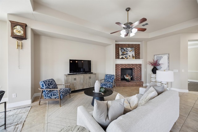 tiled living area featuring visible vents, a raised ceiling, a ceiling fan, baseboards, and a brick fireplace