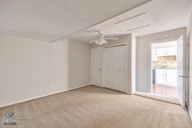 unfurnished bedroom featuring a ceiling fan, a textured ceiling, baseboards, light colored carpet, and attic access