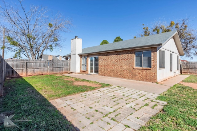 back of house with a patio, a fenced backyard, a yard, brick siding, and a chimney