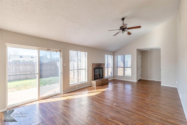 unfurnished living room with a ceiling fan, wood finished floors, a fireplace with raised hearth, vaulted ceiling, and a textured ceiling