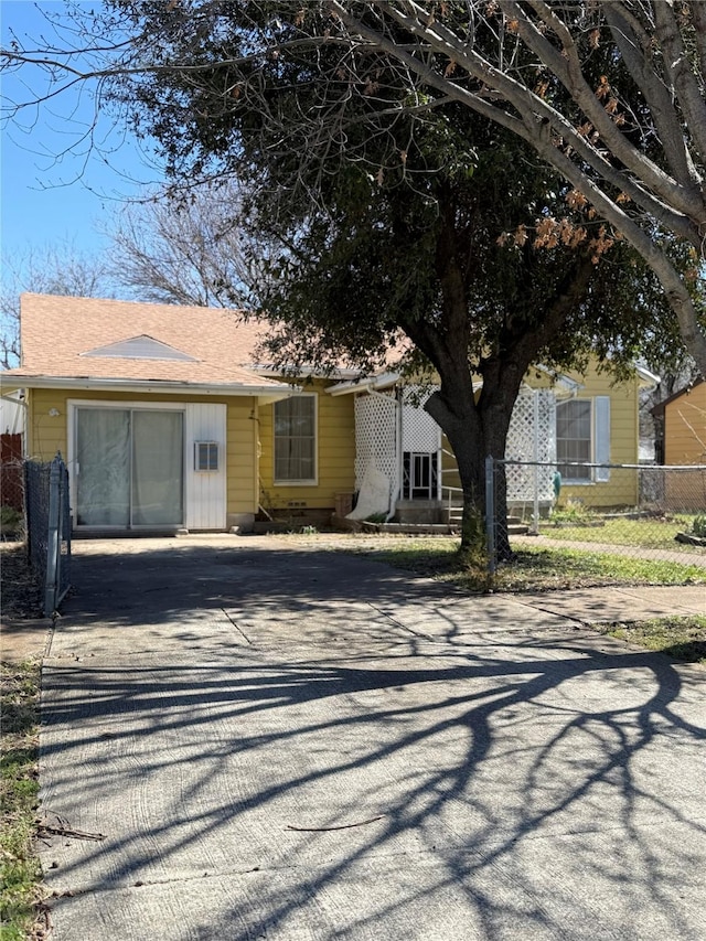 view of front facade featuring driveway, roof with shingles, and fence