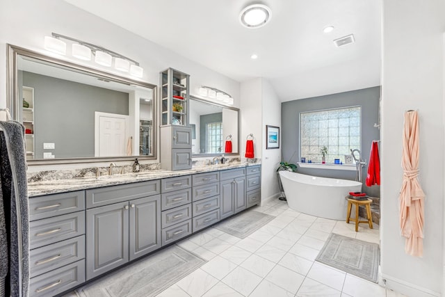 full bathroom featuring double vanity, a freestanding tub, visible vents, and a sink