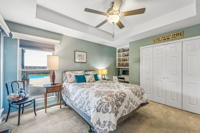 carpeted bedroom with a closet, a raised ceiling, and ceiling fan