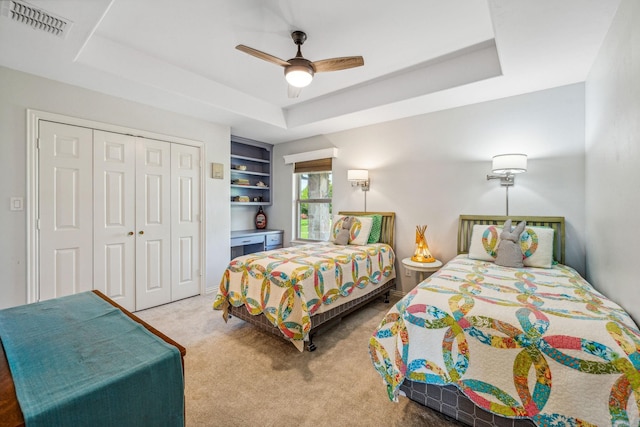 carpeted bedroom with a raised ceiling, visible vents, a closet, and ceiling fan