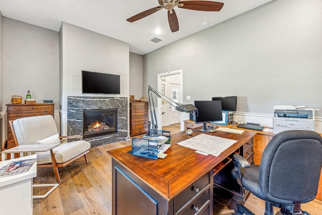 office with a wainscoted wall, visible vents, a premium fireplace, ceiling fan, and light wood-type flooring