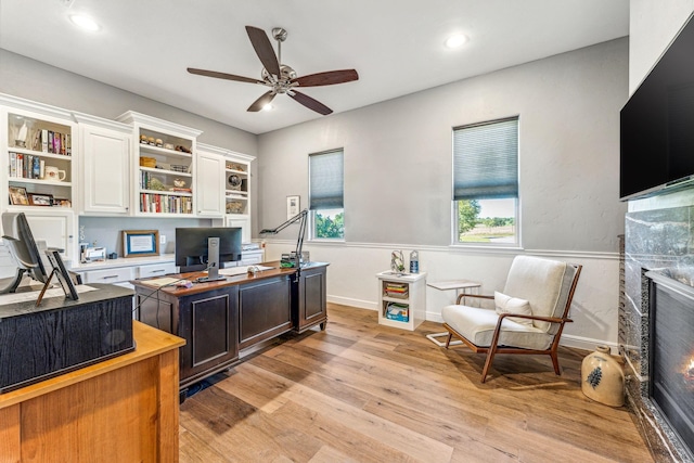 office area featuring baseboards, recessed lighting, light wood-style flooring, a glass covered fireplace, and a ceiling fan