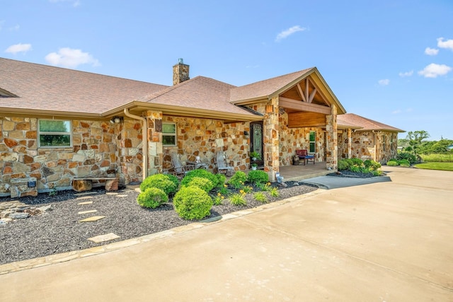 view of front of home with a shingled roof, concrete driveway, stone siding, and a chimney