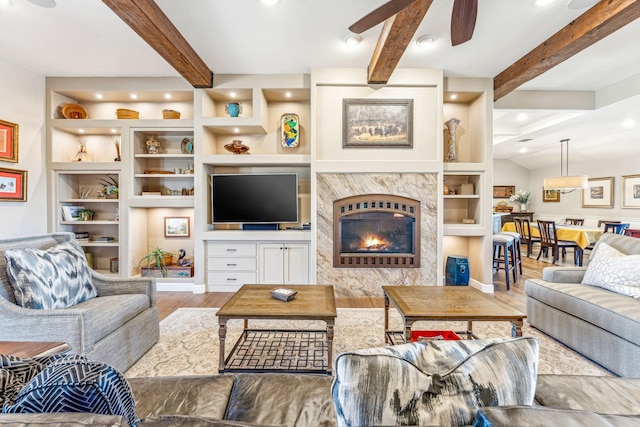 living area featuring beam ceiling, built in shelves, wood finished floors, and ceiling fan