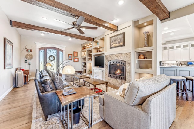 living room with beam ceiling, a ceiling fan, light wood-style floors, a premium fireplace, and baseboards