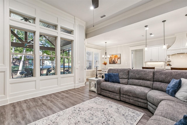 living room featuring visible vents, ceiling fan with notable chandelier, wood finished floors, crown molding, and a decorative wall