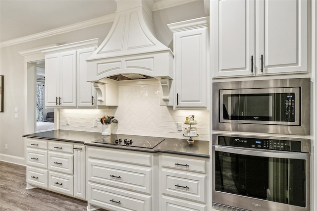 kitchen with premium range hood, dark countertops, white cabinetry, appliances with stainless steel finishes, and crown molding