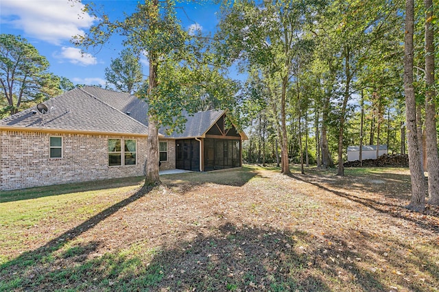 rear view of house with brick siding, a lawn, roof with shingles, and a sunroom