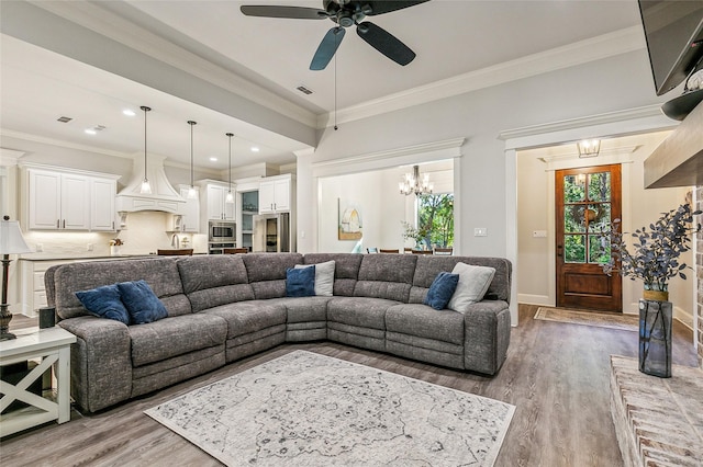 living area featuring ceiling fan with notable chandelier, crown molding, wood finished floors, and visible vents