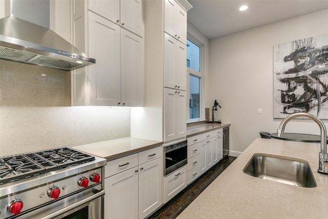 kitchen with a sink, white cabinets, wall chimney exhaust hood, light countertops, and high end range