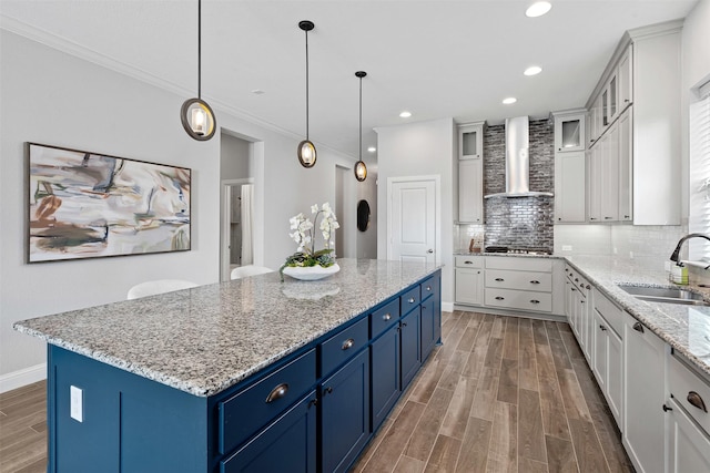 kitchen featuring wall chimney range hood, wood finished floors, blue cabinetry, and a sink