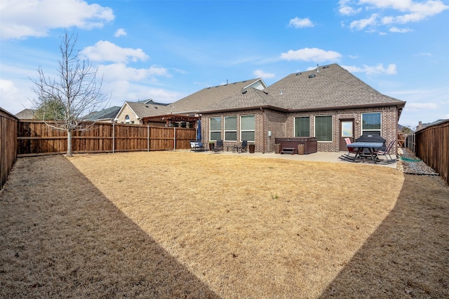 back of house featuring a fenced backyard, a patio area, a shingled roof, brick siding, and a hot tub