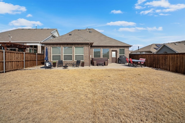 rear view of house with brick siding, a hot tub, a fenced backyard, and a patio area