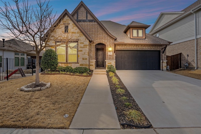 view of front of property featuring a garage, stone siding, a shingled roof, and fence