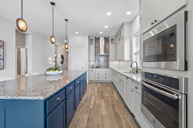 kitchen with blue cabinetry, a sink, stainless steel appliances, light wood-style floors, and wall chimney range hood