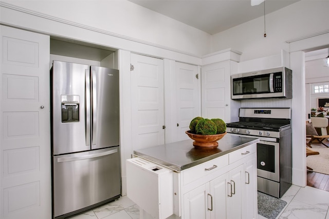 kitchen featuring marble finish floor, stainless steel countertops, a kitchen island, appliances with stainless steel finishes, and white cabinets