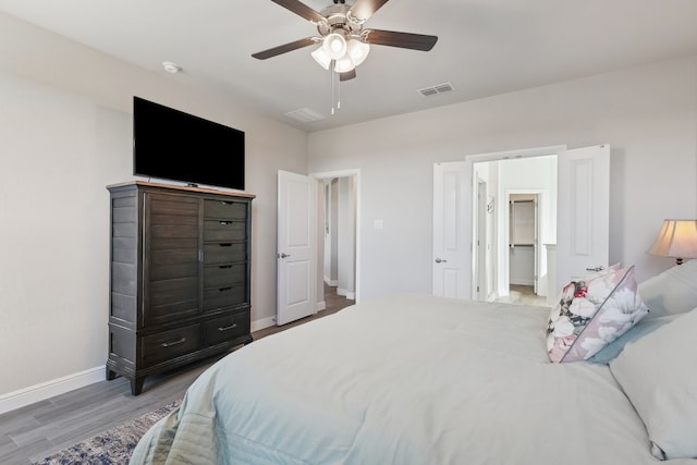 bedroom featuring visible vents, a walk in closet, a ceiling fan, wood finished floors, and baseboards