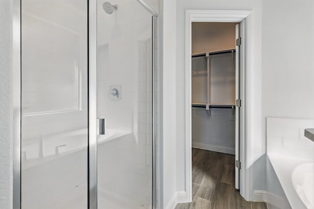 full bathroom featuring wood finished floors, a bathing tub, baseboards, a shower stall, and a walk in closet