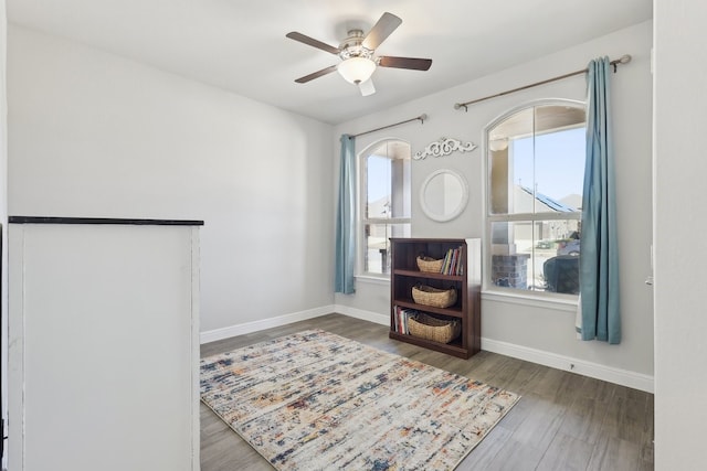 living area with a wealth of natural light, baseboards, wood finished floors, and a ceiling fan