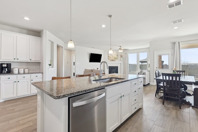 kitchen featuring visible vents, a sink, tasteful backsplash, stainless steel dishwasher, and a glass covered fireplace