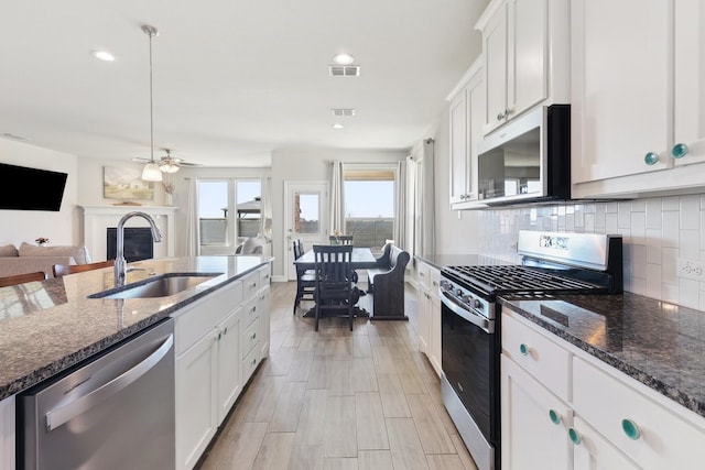 kitchen with visible vents, a sink, backsplash, a glass covered fireplace, and appliances with stainless steel finishes