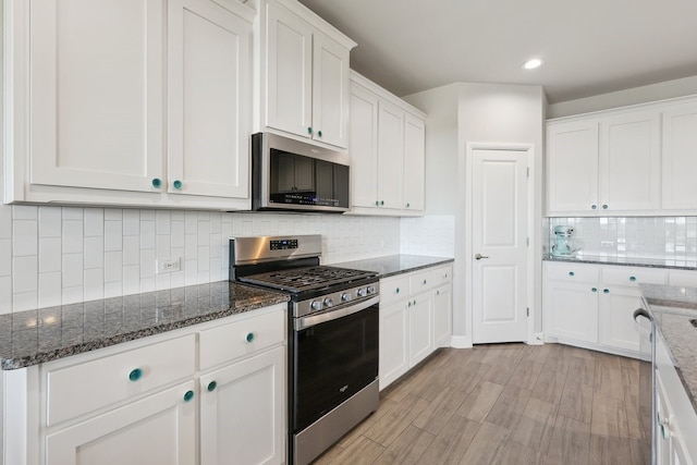 kitchen with white cabinetry, decorative backsplash, dark stone countertops, and stainless steel appliances