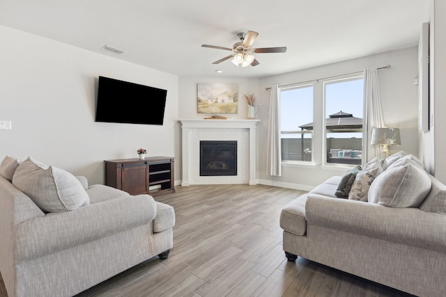 living room with visible vents, a glass covered fireplace, wood finished floors, baseboards, and ceiling fan