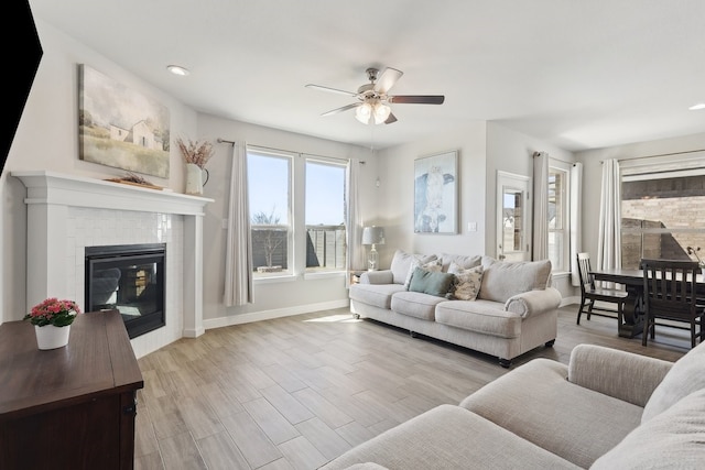 living room featuring a fireplace, a ceiling fan, light wood-type flooring, and baseboards