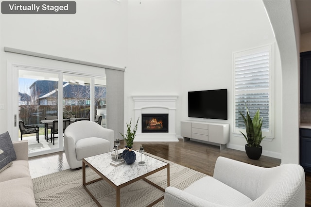 living area with a warm lit fireplace, a high ceiling, baseboards, and wood finished floors