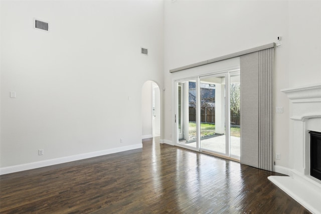 unfurnished living room with visible vents, baseboards, arched walkways, dark wood-style floors, and a glass covered fireplace