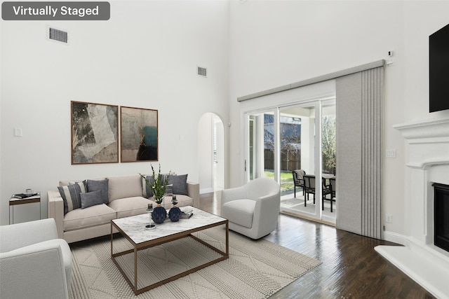 living room with visible vents, baseboards, a towering ceiling, wood finished floors, and arched walkways