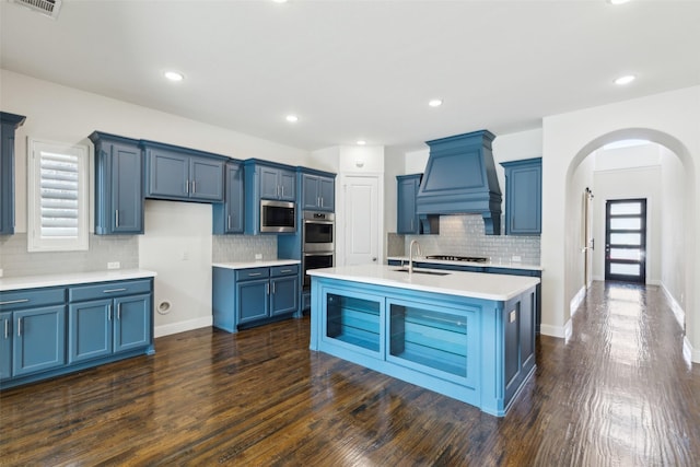 kitchen with custom exhaust hood, arched walkways, light countertops, appliances with stainless steel finishes, and blue cabinets