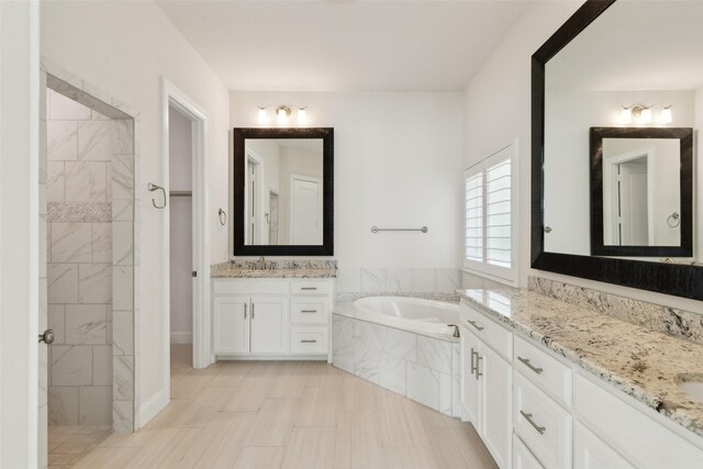 bathroom featuring a bath, tiled shower, two vanities, and a sink