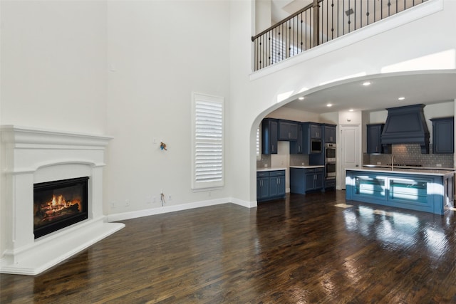 living room with a glass covered fireplace, recessed lighting, arched walkways, baseboards, and dark wood-style flooring