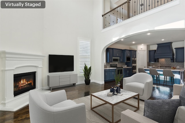 living area with dark wood-type flooring, a glass covered fireplace, recessed lighting, arched walkways, and baseboards