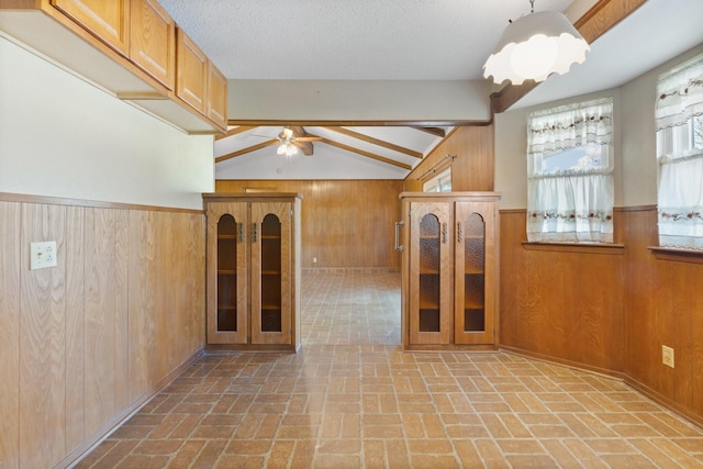 empty room with wooden walls, lofted ceiling, brick floor, wainscoting, and a textured ceiling