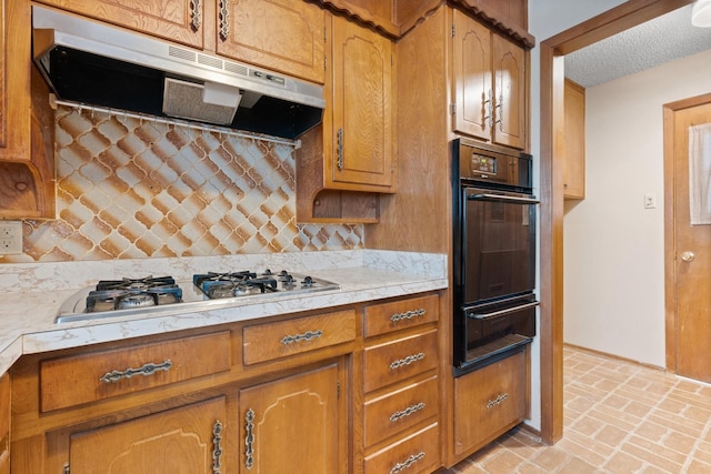 kitchen featuring a warming drawer, under cabinet range hood, stainless steel gas stovetop, light countertops, and decorative backsplash