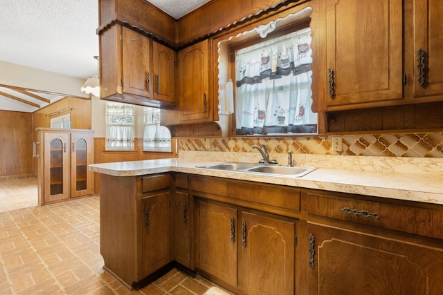 kitchen with brown cabinets, a sink, light countertops, brick floor, and decorative backsplash