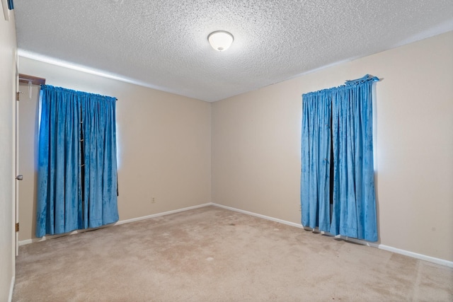 unfurnished room with baseboards, carpet, attic access, and a textured ceiling