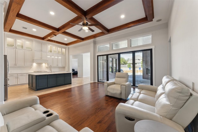 living room featuring a ceiling fan, light wood finished floors, coffered ceiling, a towering ceiling, and beamed ceiling